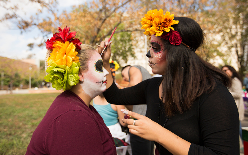 A CSUF student paints a sugar skull design on another person's face.