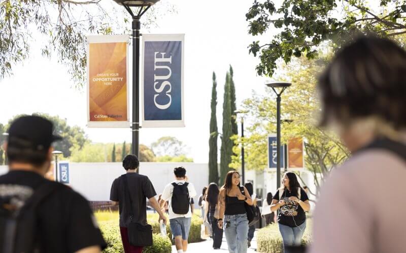 Students walk down walkway with CSUF banners and trees.