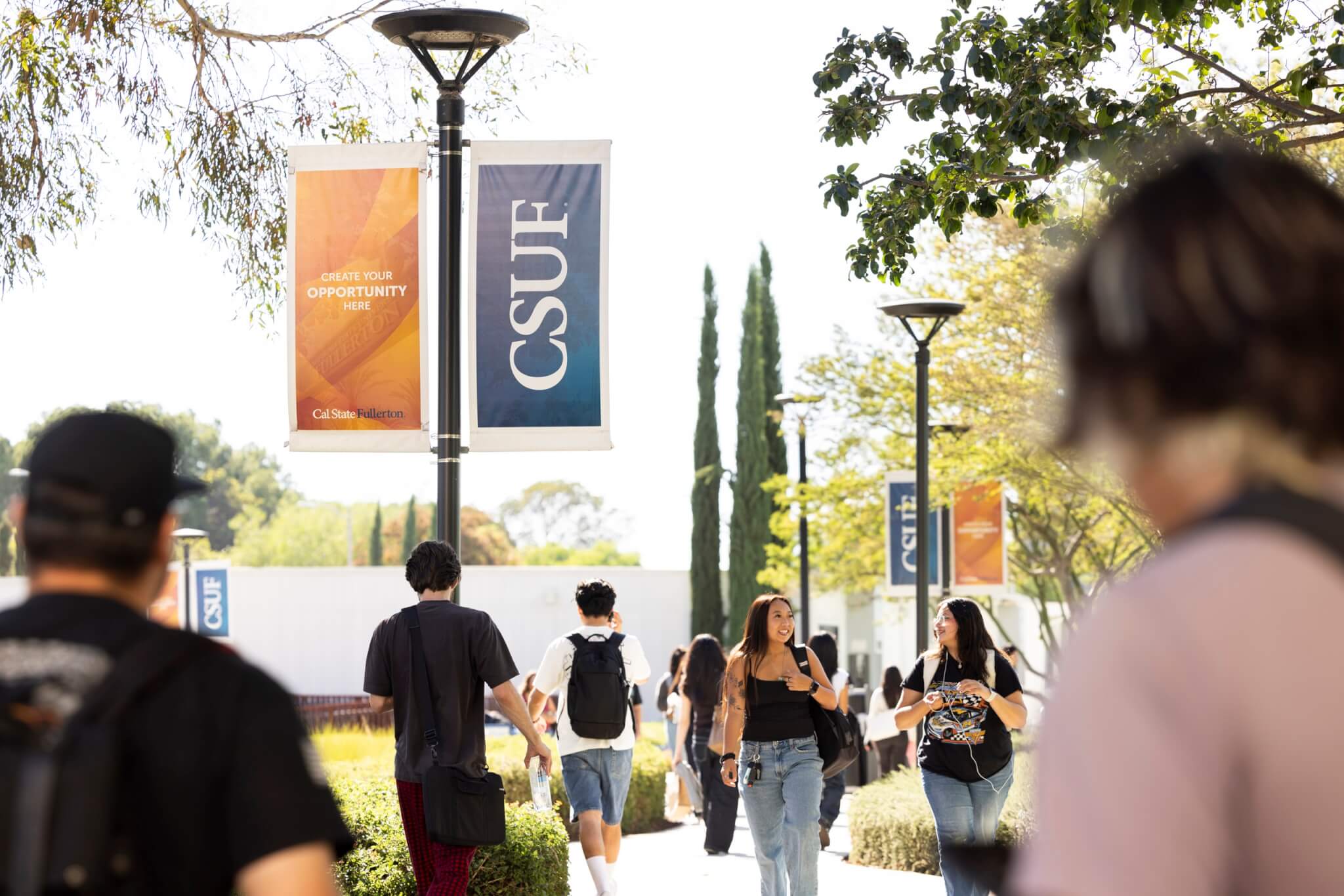 Students walk down walkway with CSUF banners and trees.