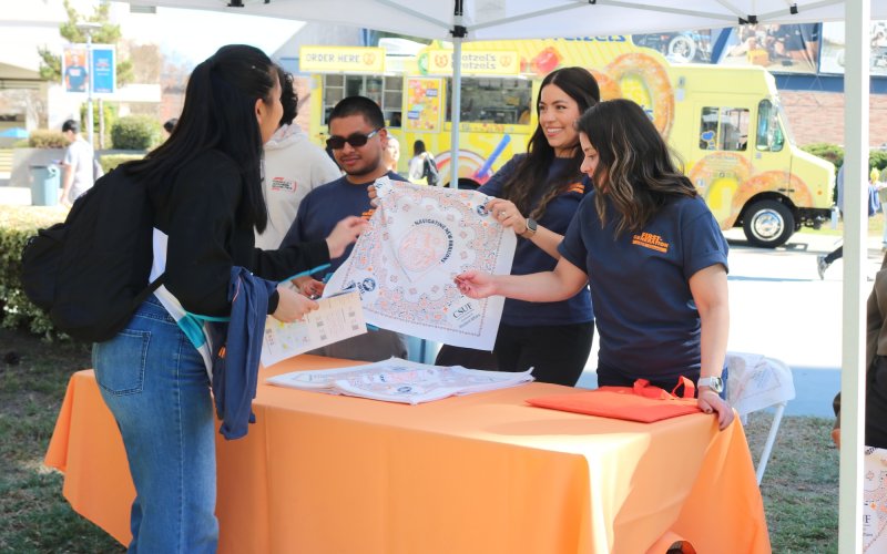 Staff tabling and student receiving information about First-Generation Week