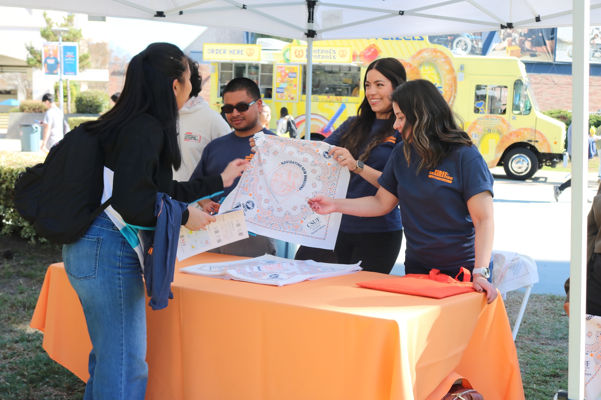 Staff tabling and student receiving information about First-Generation Week