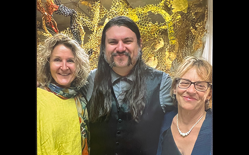 Two faculty members stand with their former student at his art exhibition.