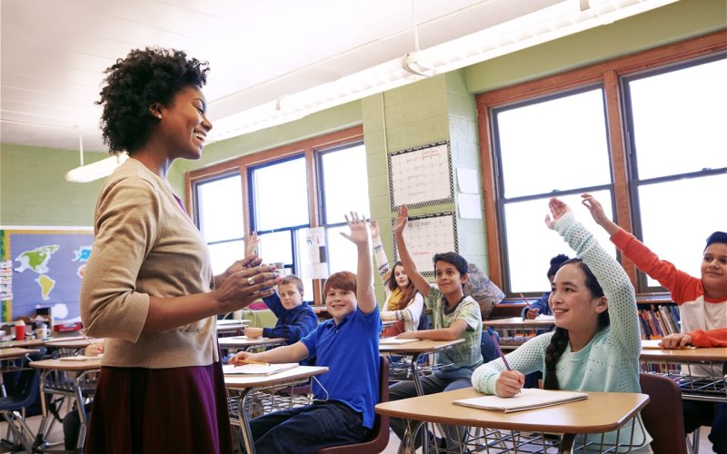 A teacher lectures a group of students who have their hands raised.