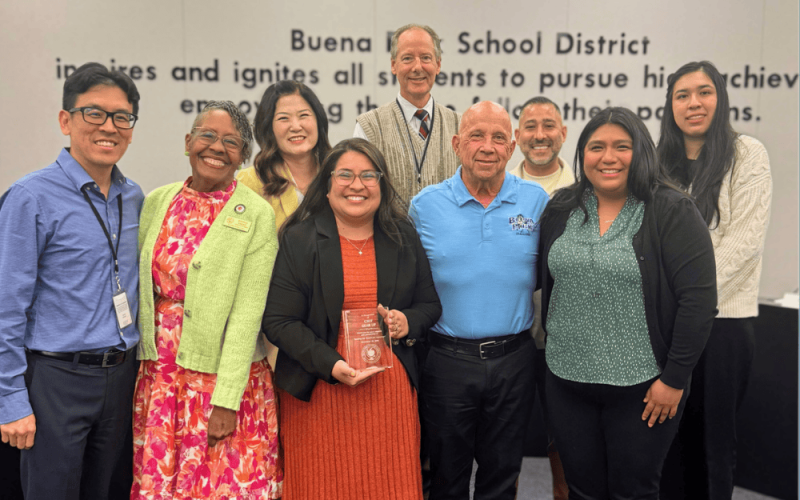 Nine professionals pose with an award in a meeting room.
