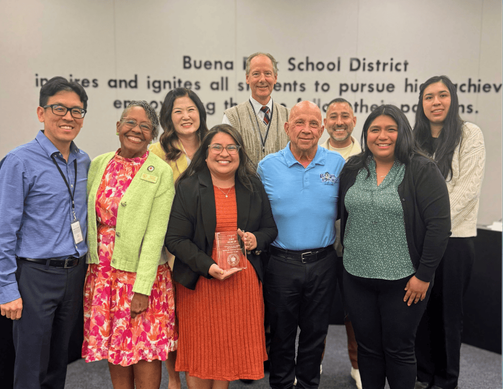 Nine professionals pose with an award in a meeting room.