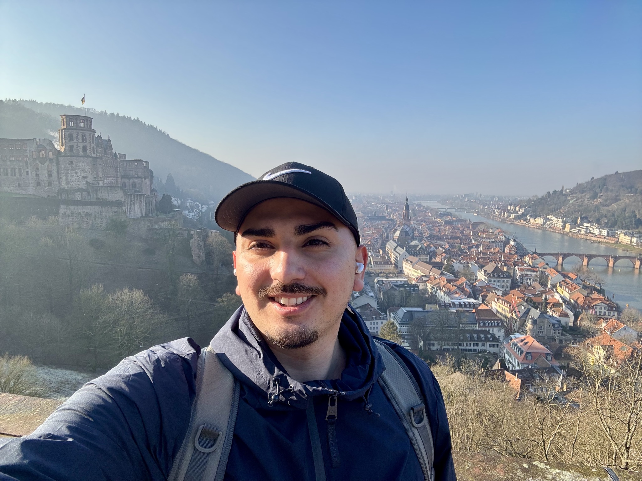 Joshua Castro smiles as he stands against a cliff overlooking a rustic city.