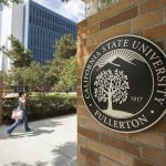A student walks past a brick pillar displaying the California State University, Fullerton seal on a sunny campus walkway.