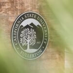 The California State University Fullerton seal mounted on an exterior wall, partially framed by blurred green foliage.