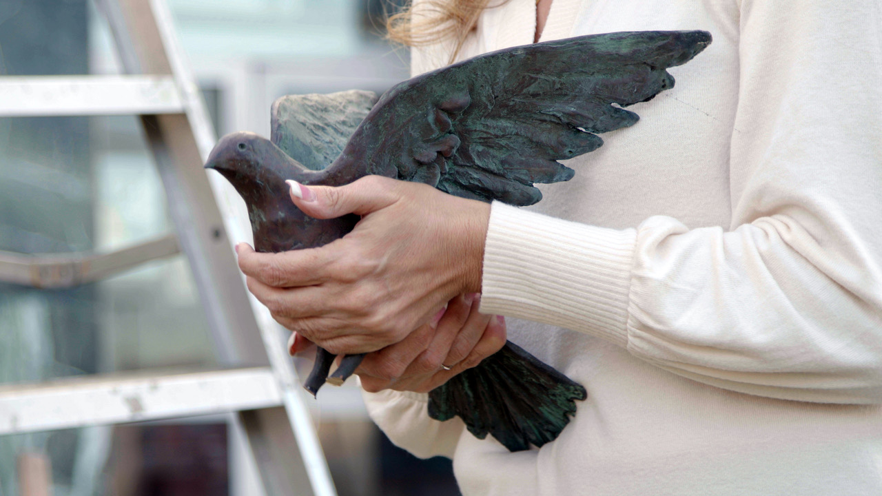Close up image of a person holding a bronze dove statue in their hands