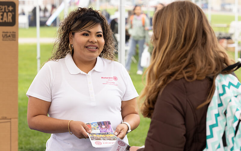 Second Start student Magaly Uriostegui holds Rotaract Club of CSUF brochure and talks to student at Discoverfest