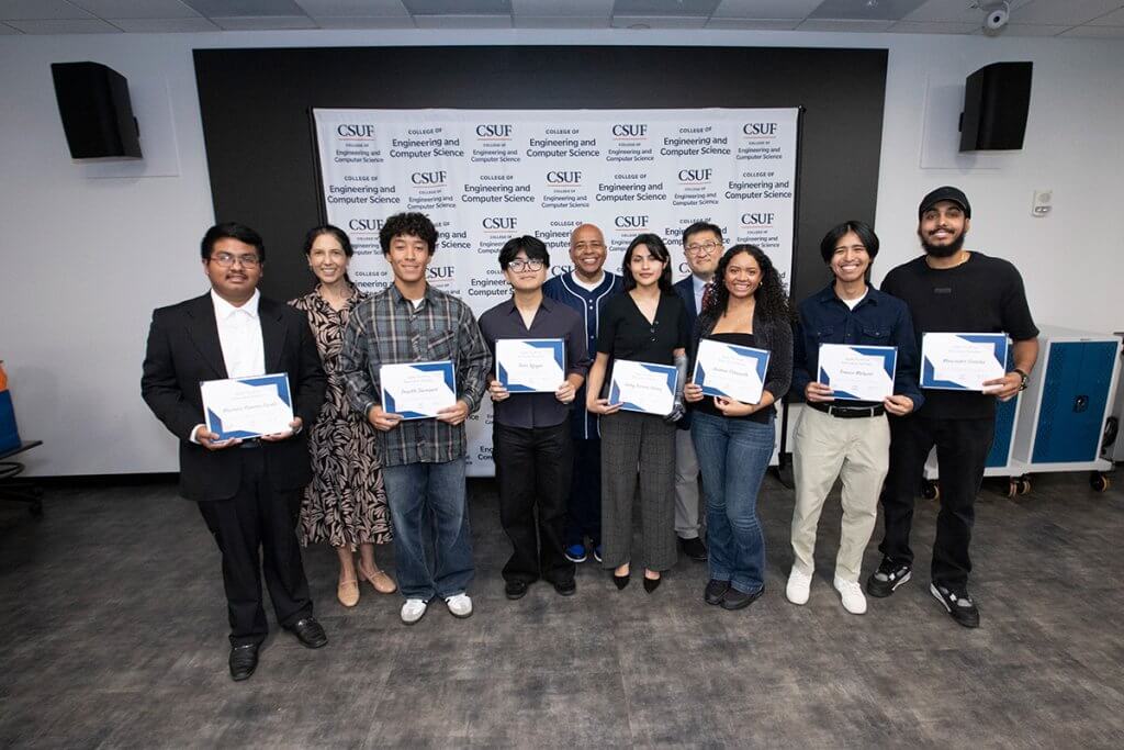 Group photo of students standing in a classroom holding certificates, with faculty members behind them in front of a College of Engineering and Computer Science backdrop.