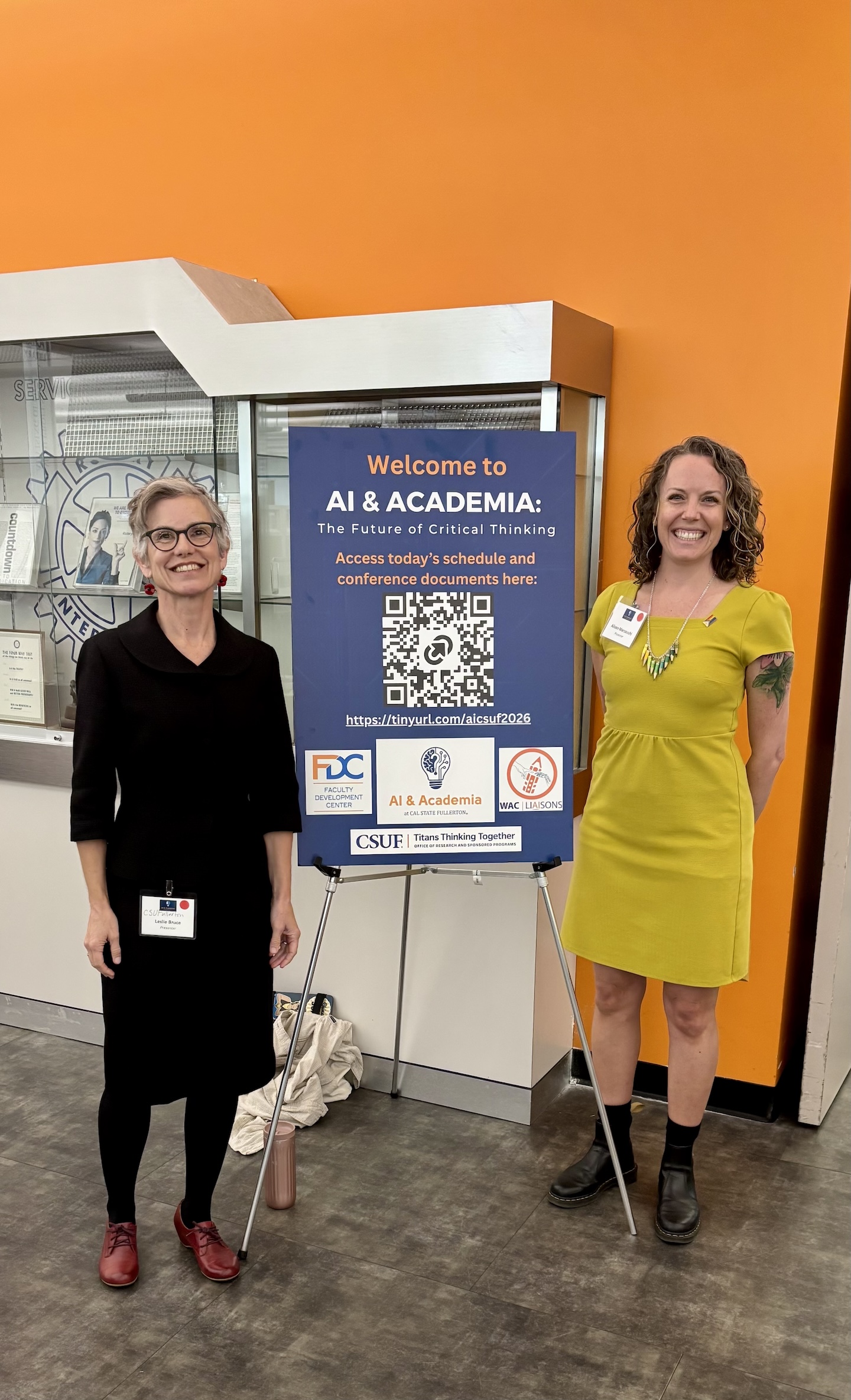 Leslie Bruce and Alison Marzocchi stand in front of an "AI and Academia" conference poster