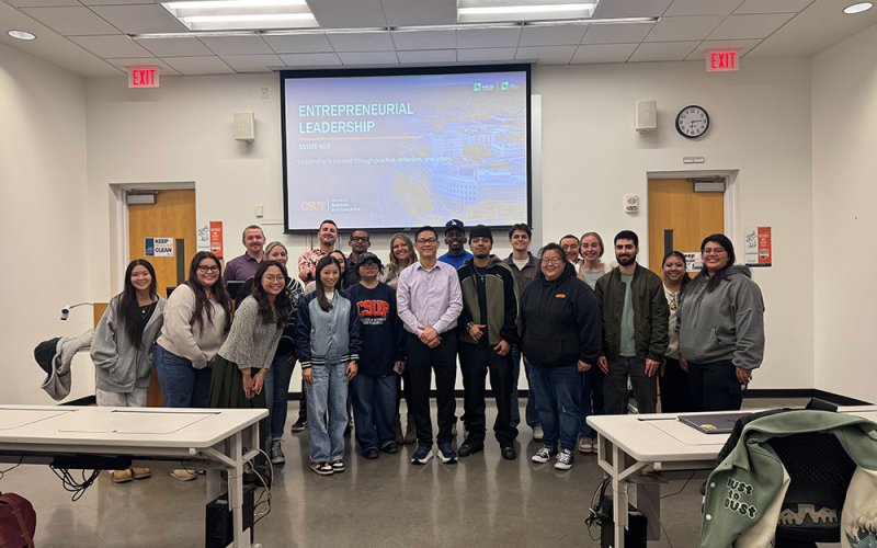 A group of students in the Entrepreneurial Leadership course pose for a group photo in front of a presentation in a classroom.
