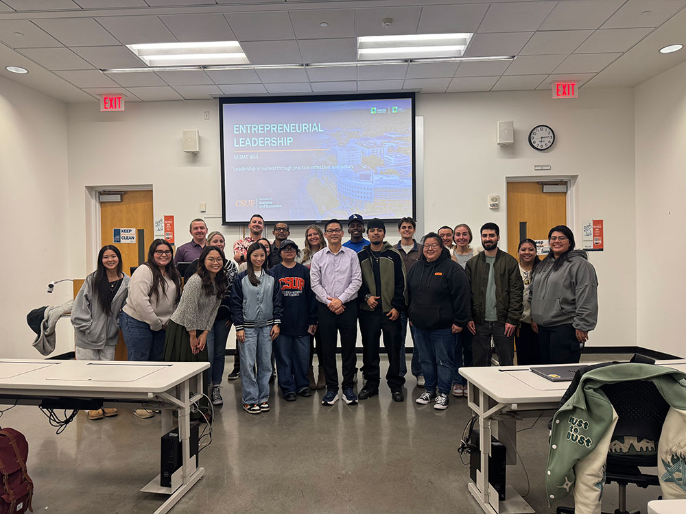 A group of students in the Entrepreneurial Leadership course pose for a group photo in front of a presentation in a classroom.