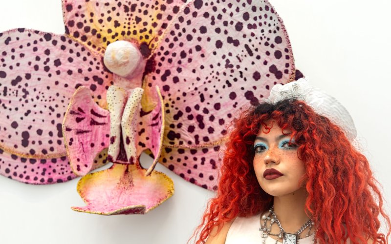 Art-teaching student Catherine “Cat” Montoya stands in front of her sculpture, "La Orquieda," which resembles a pink and maroon spotted orchid