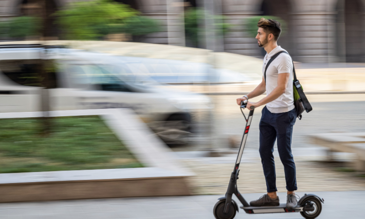 A person rides an e-scooter on the sidewalk