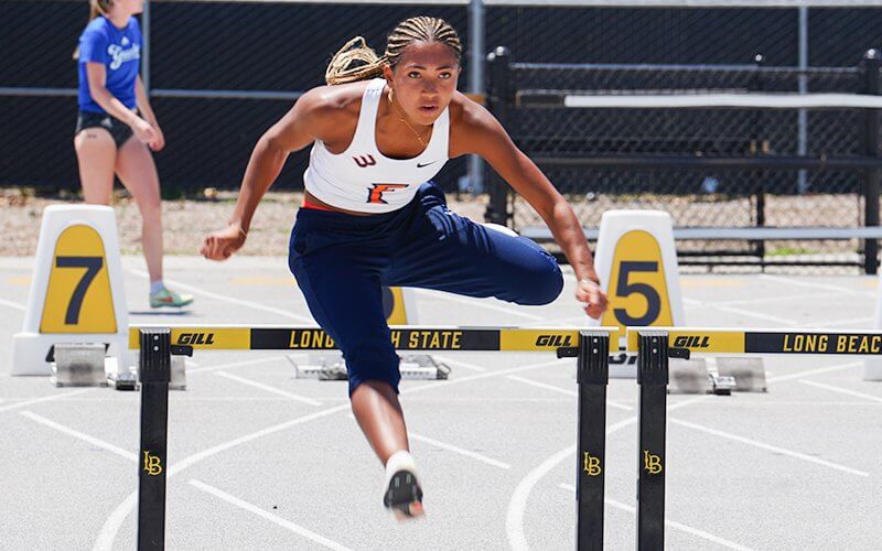 CSUF Track & Field student-athlete Maya Osola jumps over a hurdle on the track.