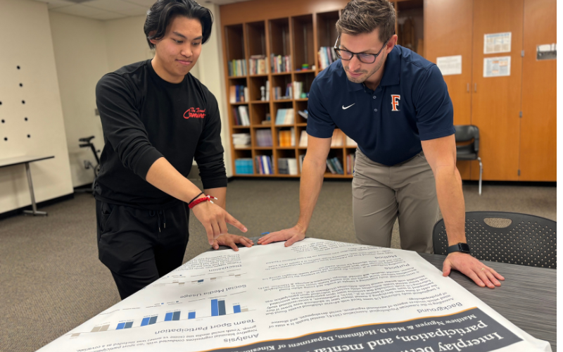 Kinesiology graduate student Matthew Nguyen and faculty member Matt Hoffmann review a research poster