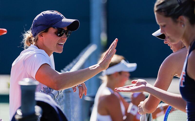 Ellie Johnson, women's tennis coach, high-fives a player on the tennis court