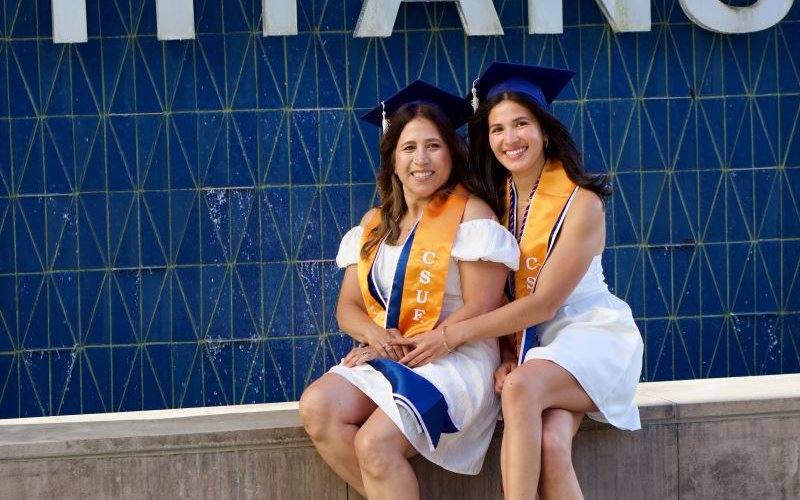 Diane and Ashlynn Viramontes wear CSUF grad regalia and pose for a photo in front of the Titans fountain.