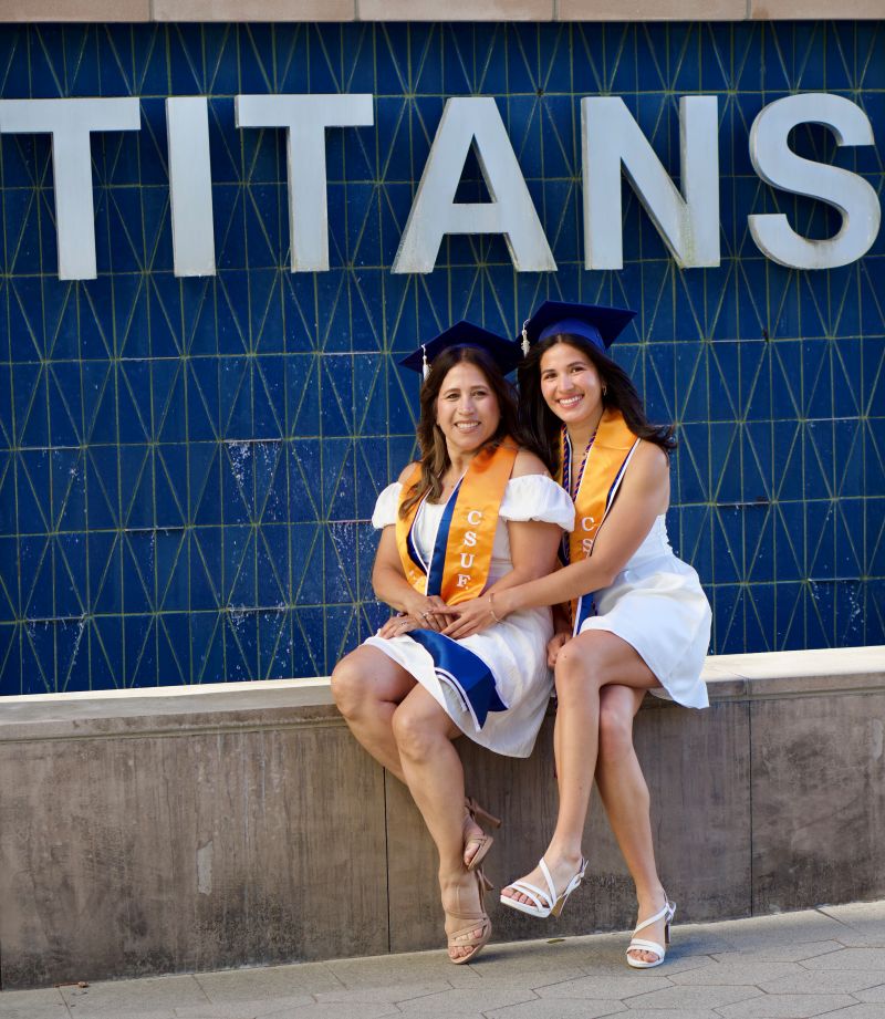 Diane and Ashlynn Viramontes wear CSUF grad regalia and pose for a photo in front of the Titans fountain.