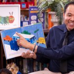 Kevin Greene holds a book and reads to a student.