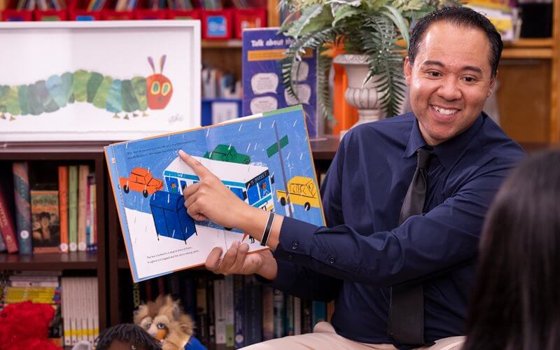 Kevin Greene holds a book and reads to a student.
