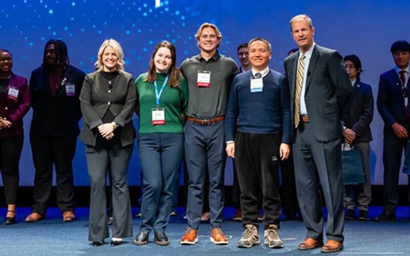 Five people stand together on stage at the 9th Annual Lockheed Martin Ethics in Engineering Case Competition.