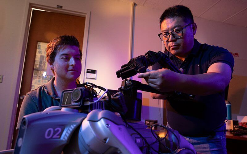 Computer science student Mason Jennings and professor Yu Bai work on a robotic dog project.