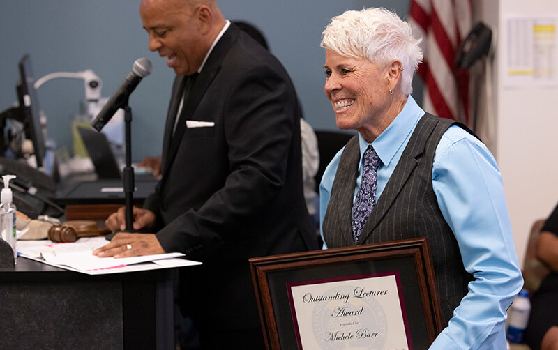 Michele Barr smiles and holds award at the April 23 Academic Senate meeting.