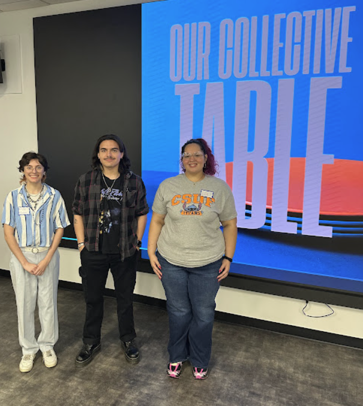 Three students stand in front of a presentation screen that reads, "Our Collective Table."