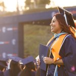 A graduate smiles and holds her certificate at CSUF's 2026 Commencement