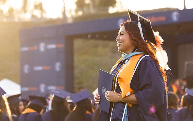 A graduate smiles and holds her certificate at CSUF's 2026 Commencement