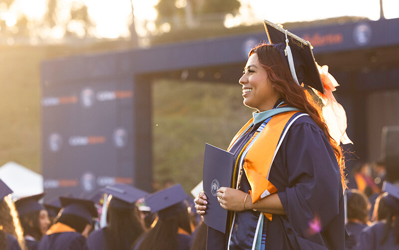A graduate smiles and holds her certificate at CSUF's 2026 Commencement