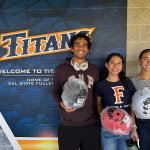 Three Cal State Fullerton students hold bicycle helmets during a campus giveaway event to promote e-vehicle safety