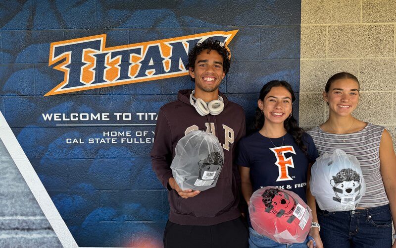 Three Cal State Fullerton students hold bicycle helmets during a campus giveaway event to promote e-vehicle safety