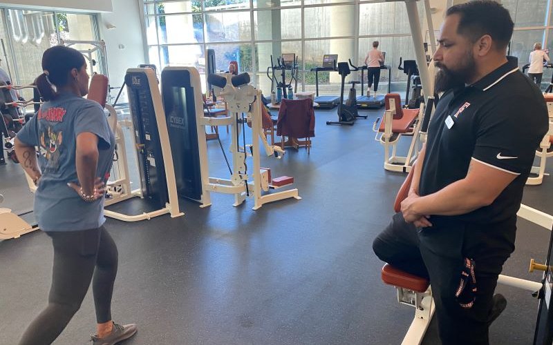 Graduate student guides Employee Wellness Program member through a strength exercise.