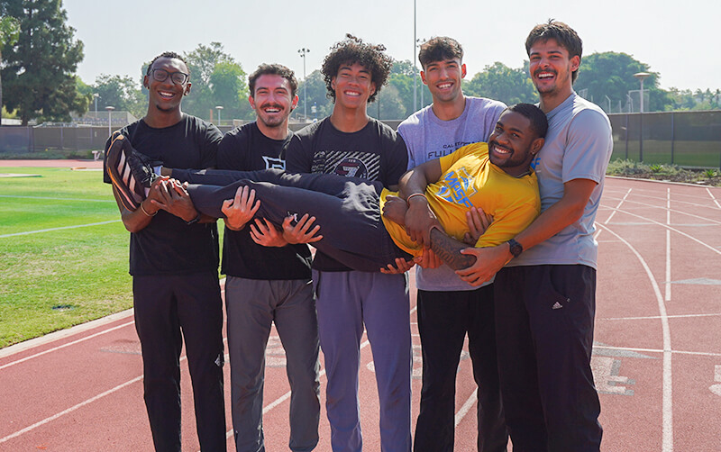 Student-athletes Ian Dossman, Maleik Pabon, Dominic Gates, Isaiah Emerson, Abel Jordan and Keith Orona stand on a track field.