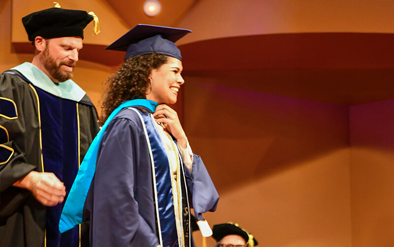 Graduate student participates in HSS hooding ceremony in Meng Concert Hall.