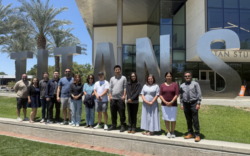 A group of CSUF faculty pose in front of the Titans letters on campus.