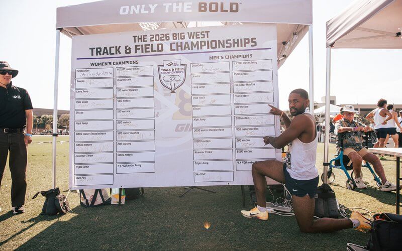 Ian Dossman kneels by the results board at the 2026 Big West Track & Field Championships.