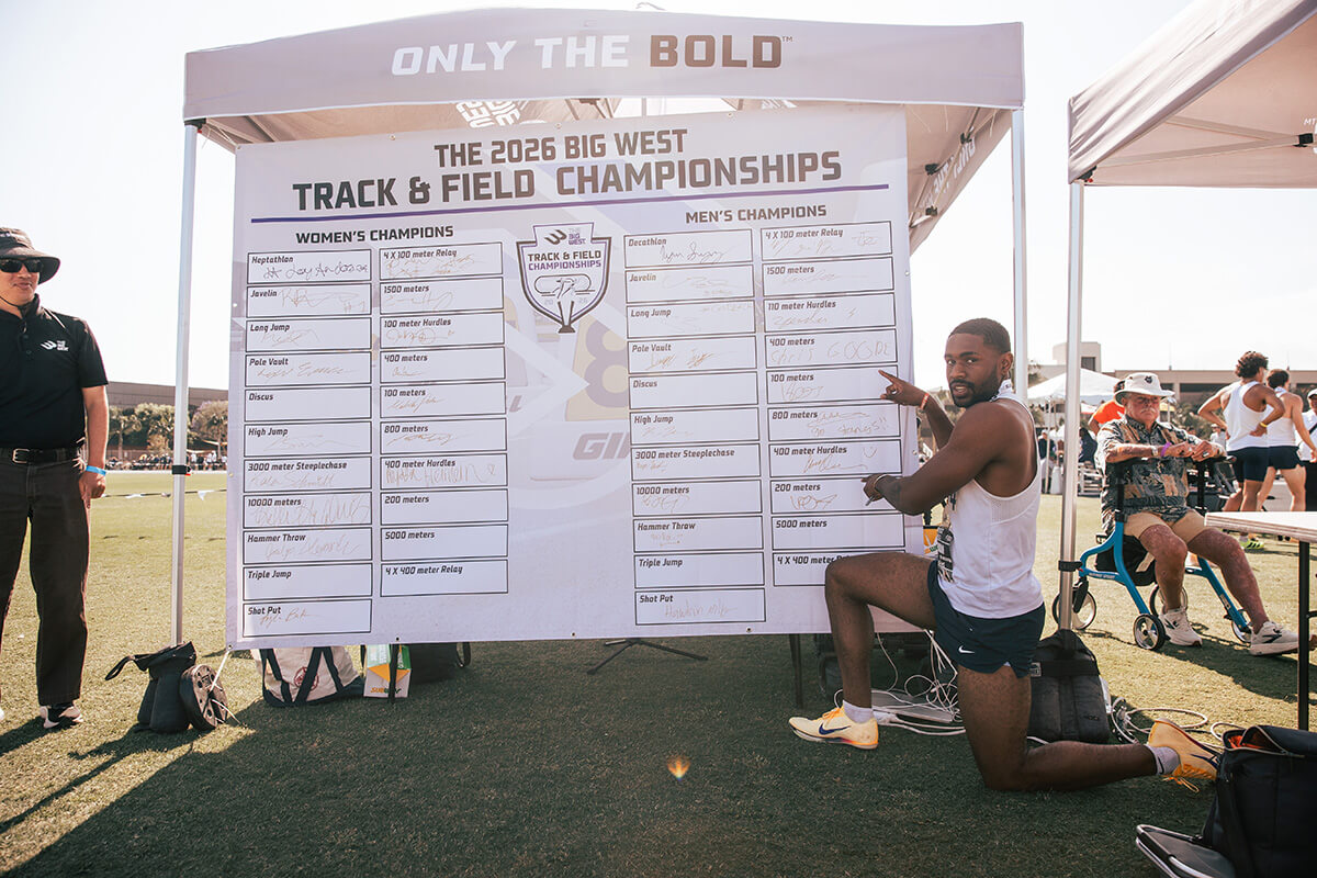 Ian Dossman kneels by the results board at the 2026 Big West Track & Field Championships.