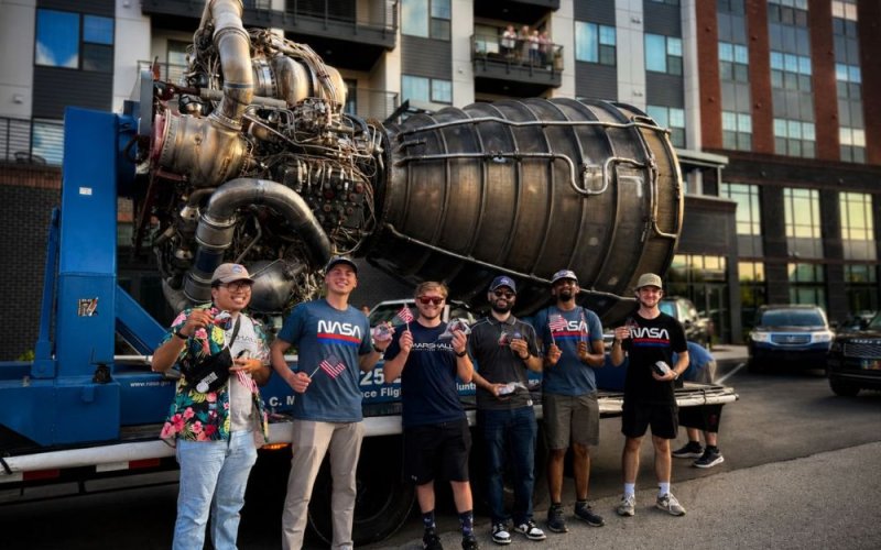 CSUF business alum Abraham Mohammad stands in front of a rocket engine with fellow NASA interns.