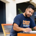 A student writes in a notebook in front of the Engineering Building.