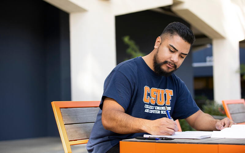 A student writes in a notebook in front of the Engineering Building.