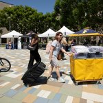 A family moves a rolling bin on the housing piazza.