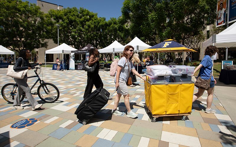 A family moves a rolling bin on the housing piazza.
