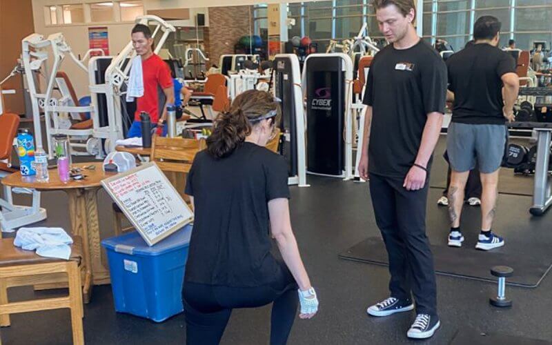 A kinesiology student guides an employee through an exercise routine in the gym.