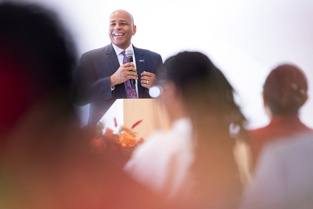 CSUF President Ronald Rochon stands behind a podium and speaks to local college leaders.